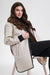 A woman seated on a chair wearing a long quilted cream-colored coat with hood from Nikki Jones