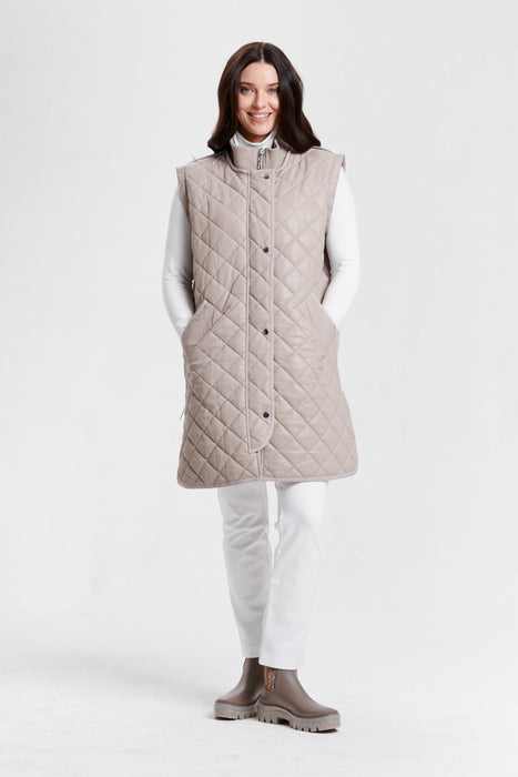 A woman modeling a taupe-colored quilted mid-length coat with a high collar convertible to a vest from Nikki Jones