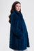 A woman wearing a plush, quilted faux fur coat in a teal blue color with side pockets from Nikki Jones