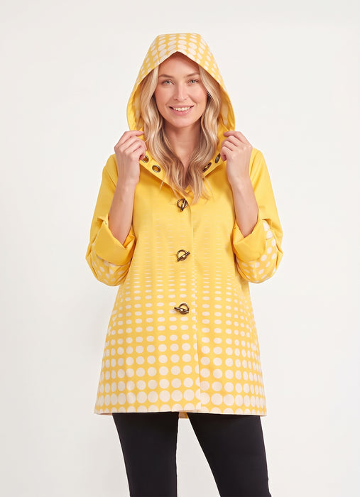 Woman wearing the Oopera Yellow Polka Dot Reversible Toggle Raincoat with a vibrant ombre pattern, adjustable hood, and lightweight water-repellent fabric.