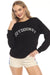 Woman wearing a black top with 'OUTDOORSY' text embroidery with crew neck and long sleeves