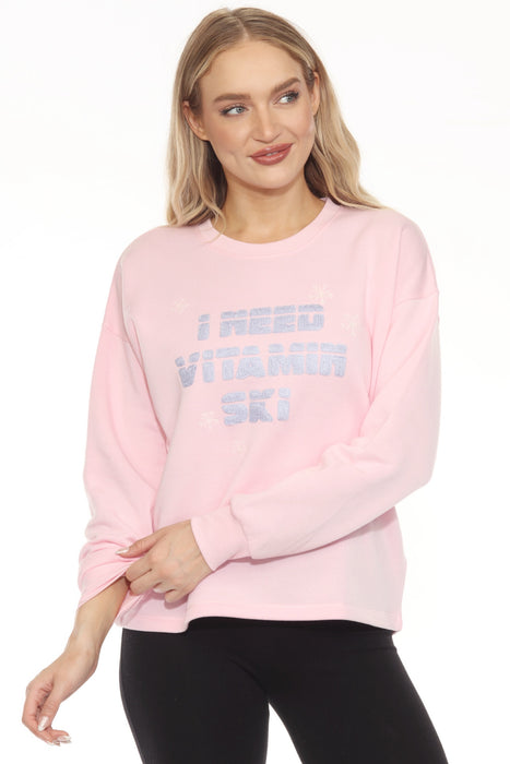 Woman wearing a pink sweatshirt with "I Need Vitamin Ski" text embroidery